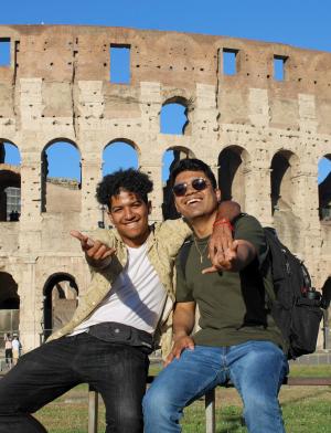 two male students pose for a fun photo in front of the Roman Colosseum in Italy
